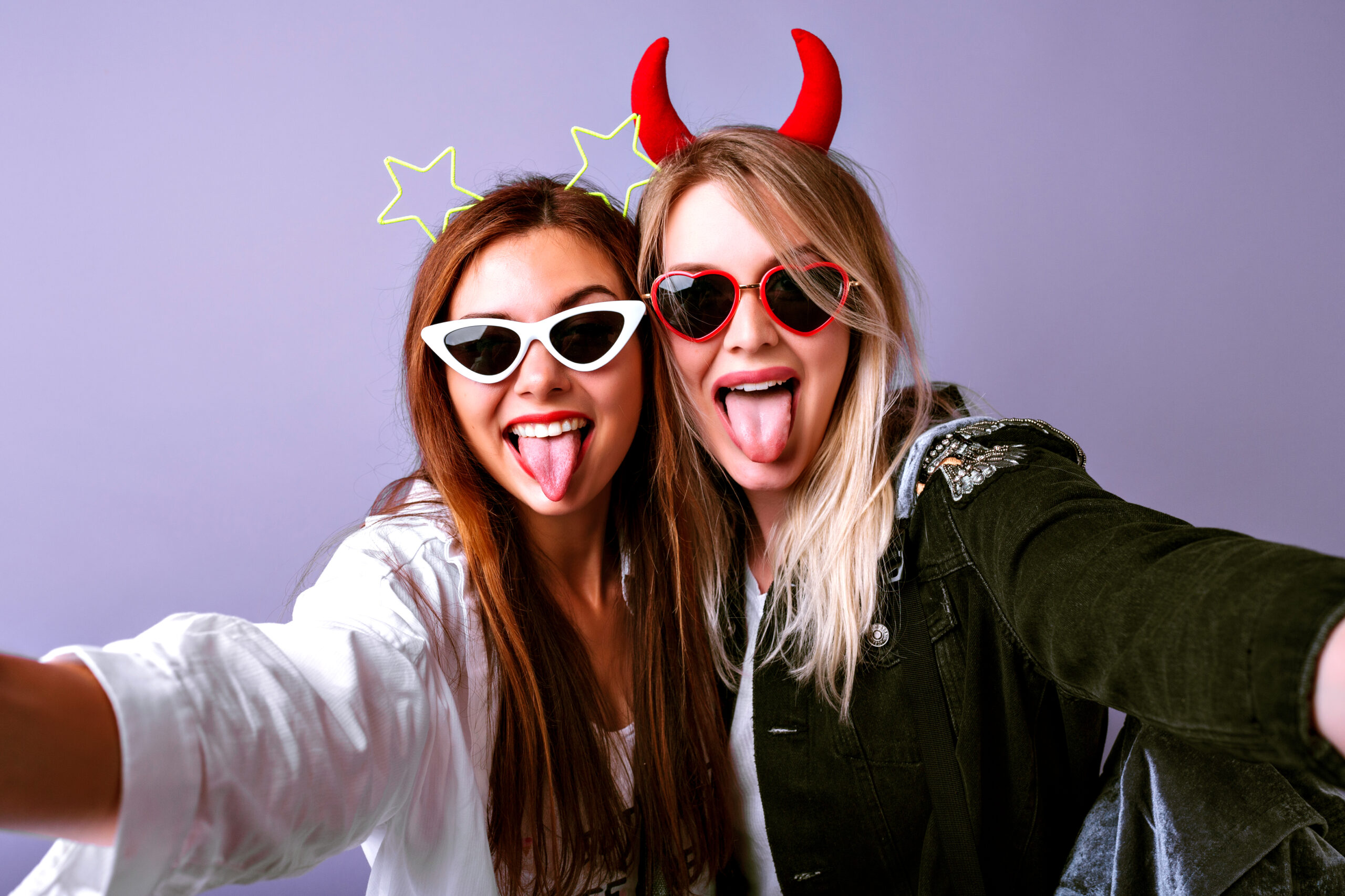 Young funny girls making selfie at studio making grimaces and going crazy, vintage glasses, devil and stars party hair bands, casual youth clothes, positive mood.